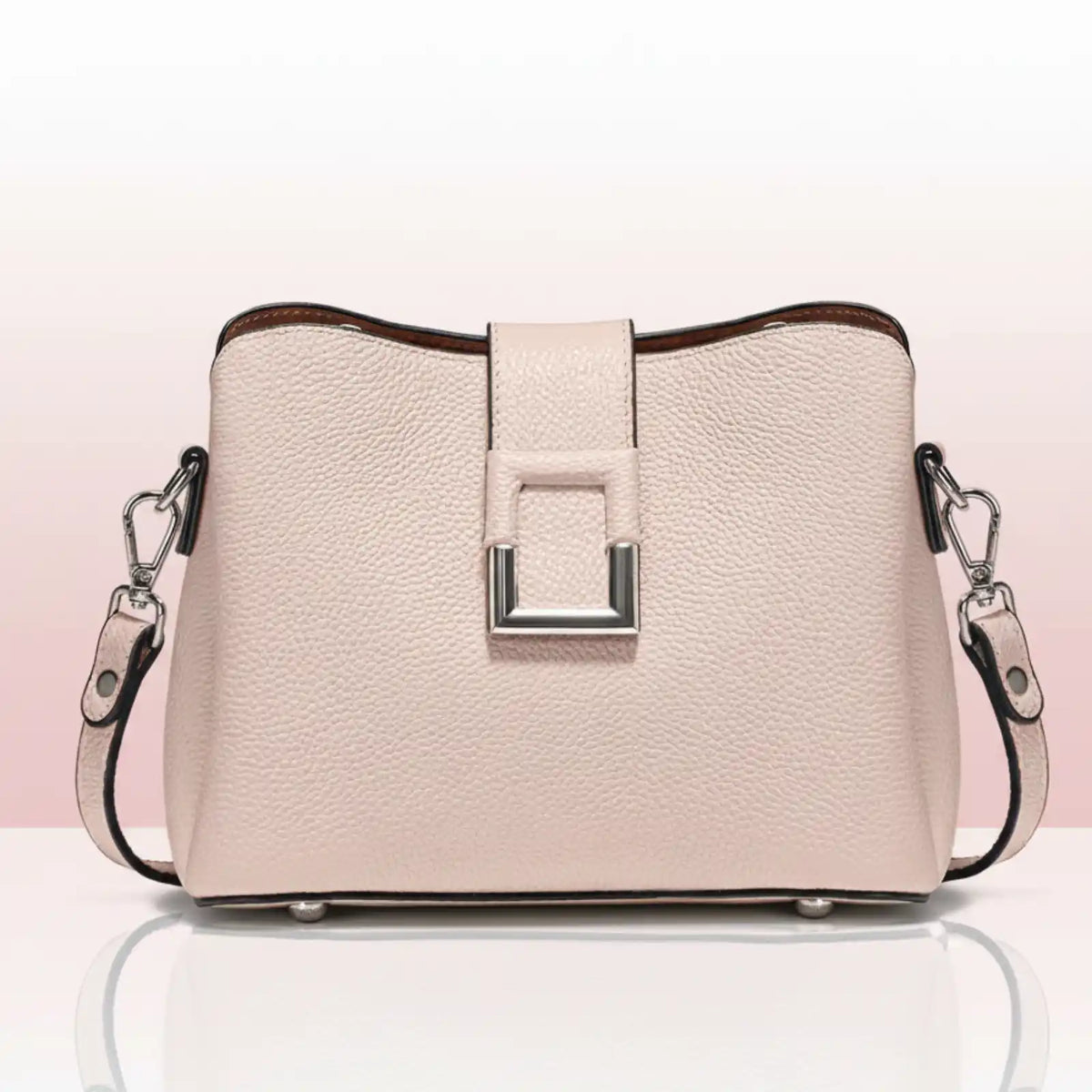 The main subject is a light pink handbag with a textured surface. It has a rectangular metal clasp in the center, a brown