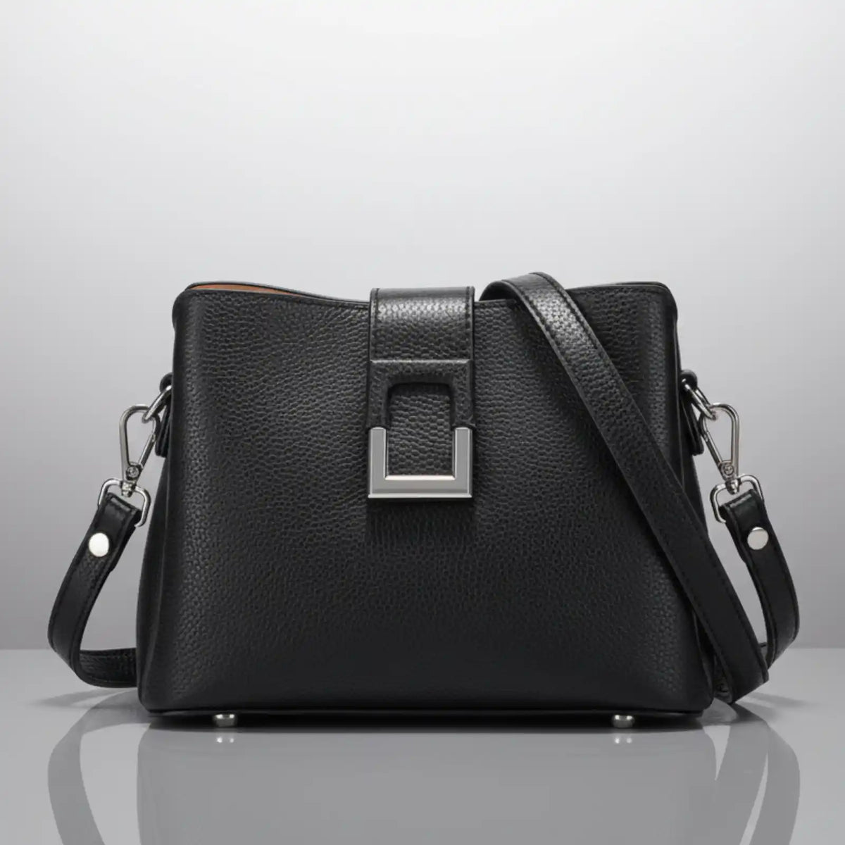 The main subject is a black handbag. It has a textured leather-like surface, a rectangular metal clasp in the center, and a